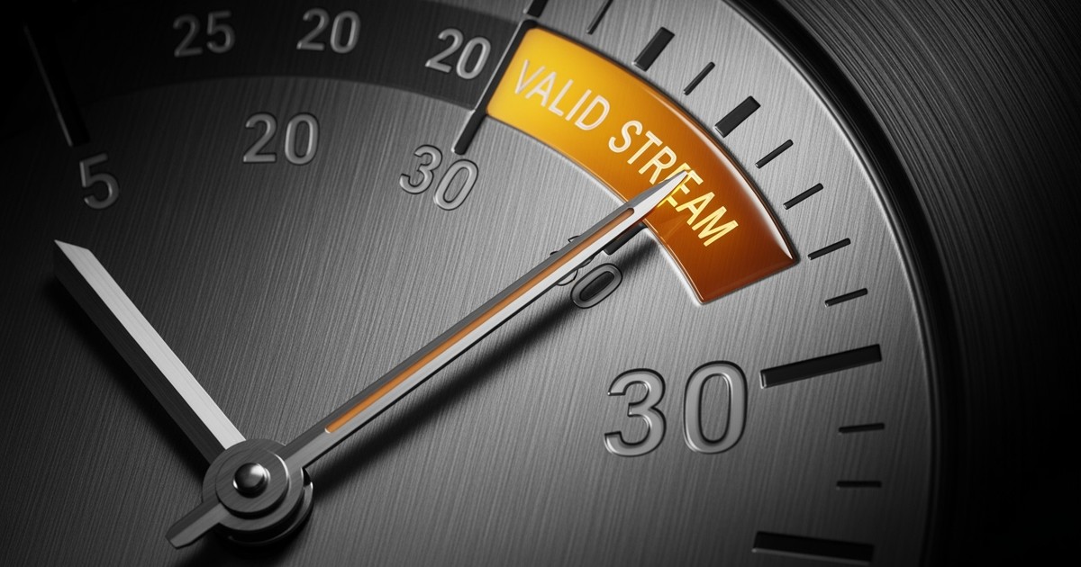 Macro shot of a luxury analog gauge where a needle crosses a glowing amber threshold marked 30, symbolizing the streaming count rule.